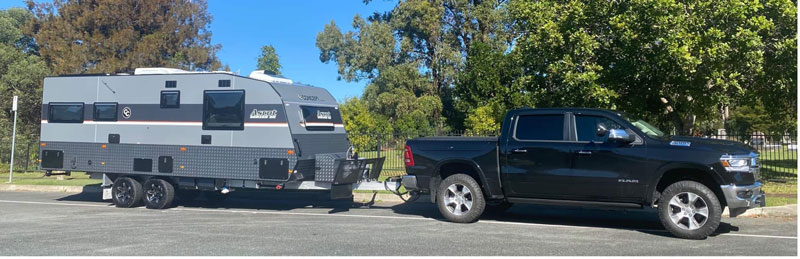 Black pickup truck towing a large grey caravan in a sunny lot.